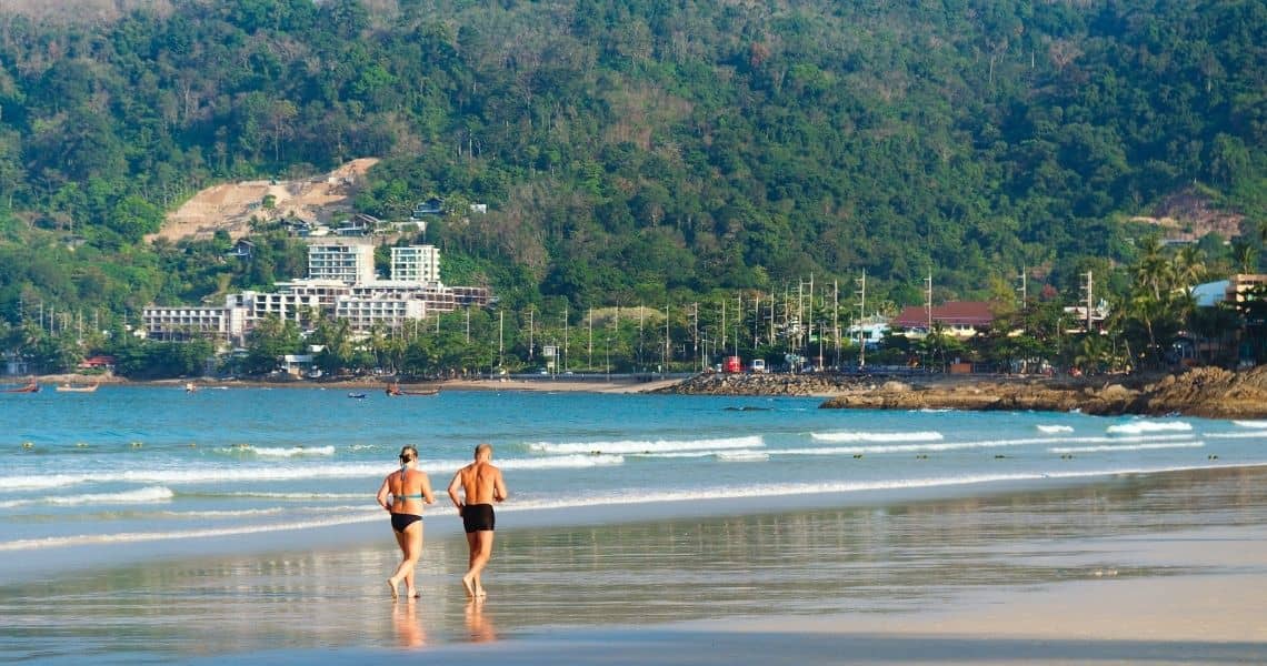 Promisecare Medical Group - Two people enjoying a spring fitness walk on a beach with a coastal resort in the background.