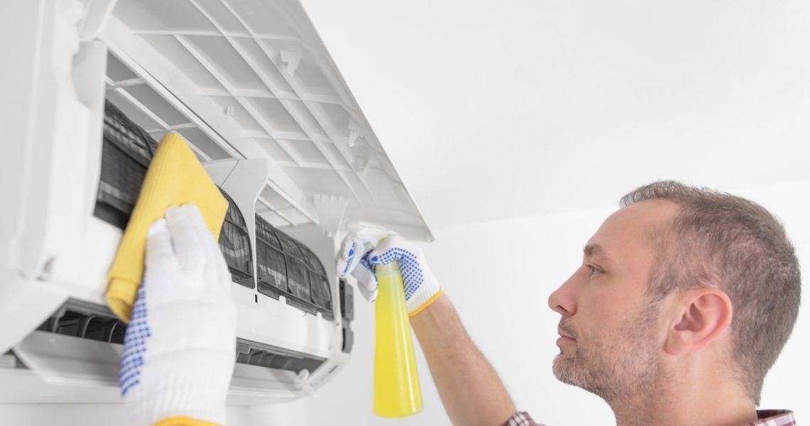 Promisecare Medical Group - A person cleaning an air conditioning unit with a cloth and spray bottle.