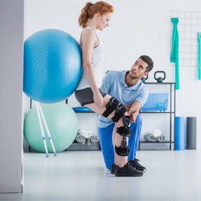 Promisecare Medical Group - Rehabilitation therapist helping a woman with a knee brace.