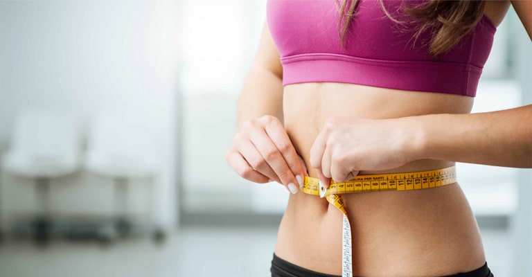 Promisecare Medical Group - A woman measuring her waist with a measuring tape as part of her weight loss journey.