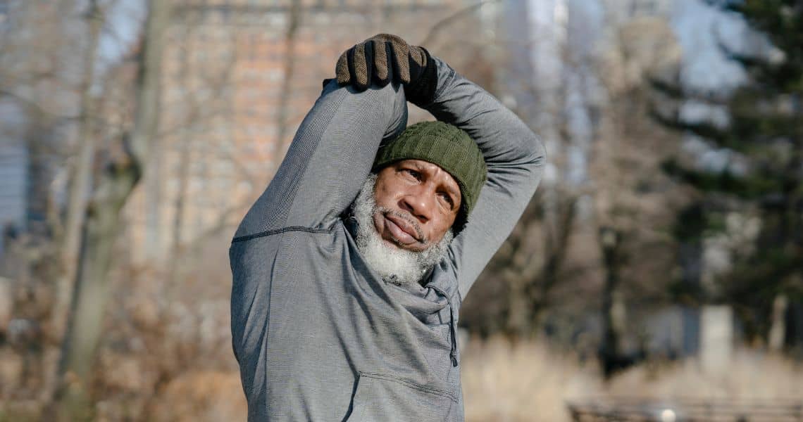 Promisecare Medical Group - An elderly man is stretching his arms in a park.