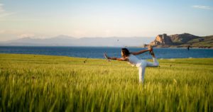 Promisecare Medical Group - A woman practicing yoga in a field near the ocean.