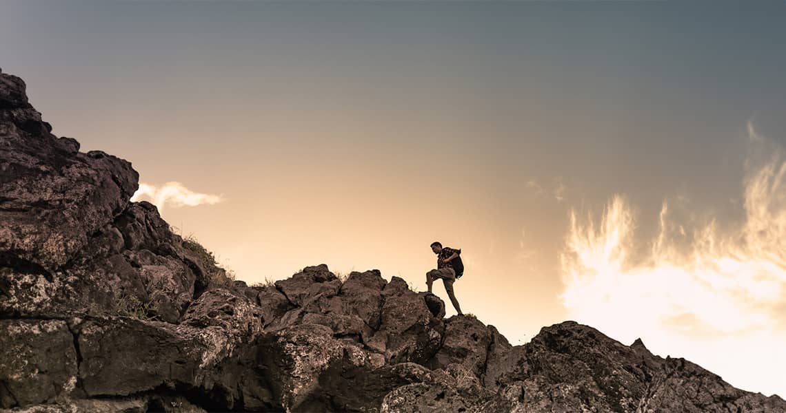 Promisecare Medical Group - A man standing on top of a rocky mountain at sunset.