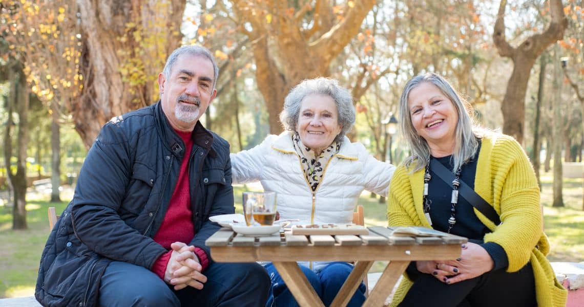 Promisecare Medical Group - Three older people sitting at a picnic table in a park.