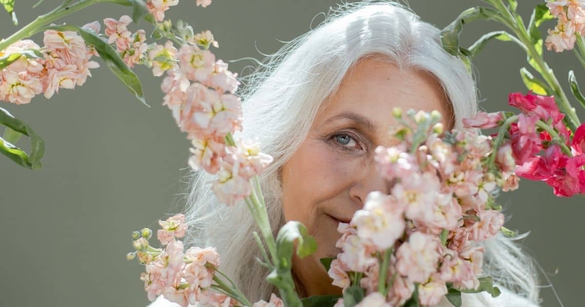 Promisecare Medical Group - Elderly woman peeking through a frame of pastel flowers.