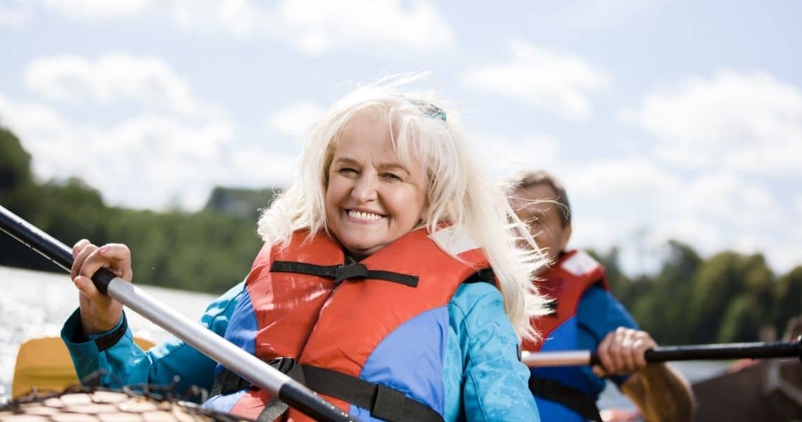 Promisecare Medical Group - Senior woman smiling while kayaking on a sunny day, experiencing a rejuvenating routine.