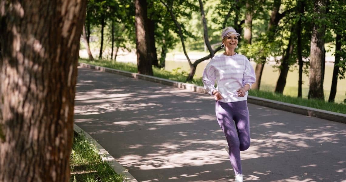 Promisecare Medical Group - A smiling woman in sportswear enjoys a spring fitness jog along a tree-lined path.