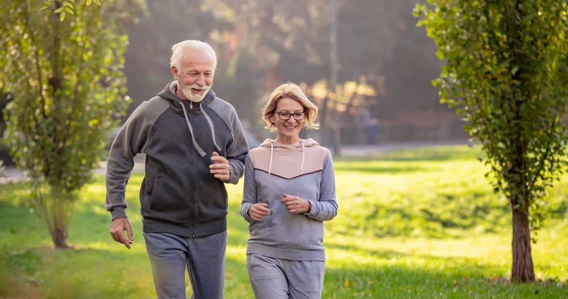 Promisecare Medical Group - Senior couple rejuvenating their routine by jogging together in a park during spring fitness.
