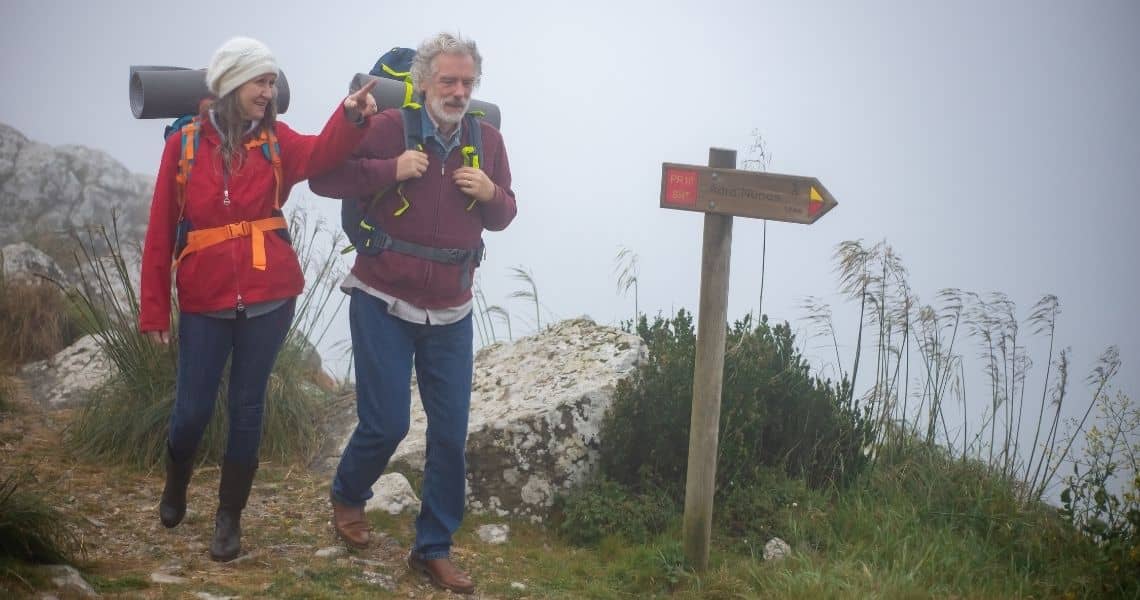 Promisecare Medical Group - Two hikers with backpacks, embarking on their spring fitness revival, walking by a trail signpost in foggy conditions.
