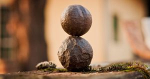 Promisecare Medical Group - Two round stones stacked vertically on a mossy surface with a softly blurred background.