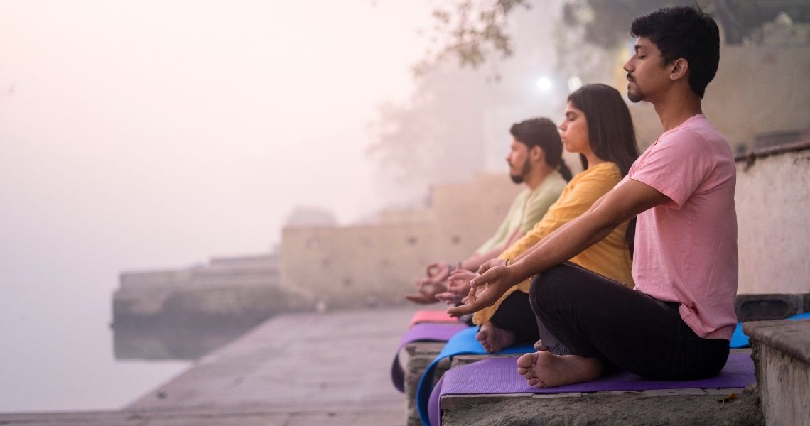 Promisecare Medical Group - Three people meditating on mats by a misty riverside at dawn.