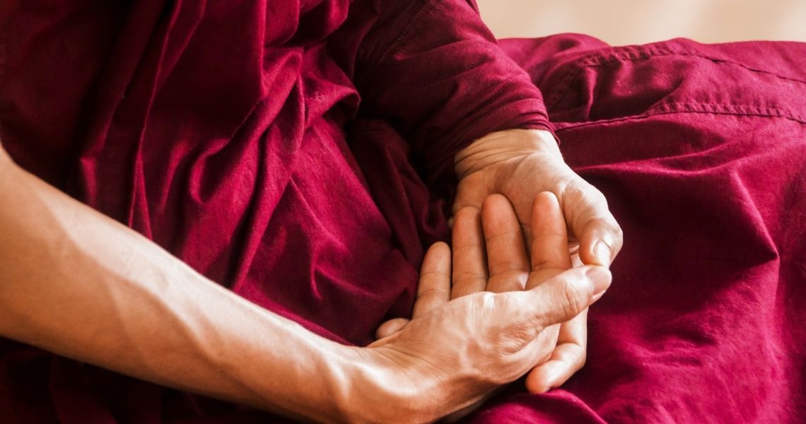 Promisecare Medical Group - Close-up of two hands clasped together, one resting on the other, with both wearing deep red robes.
