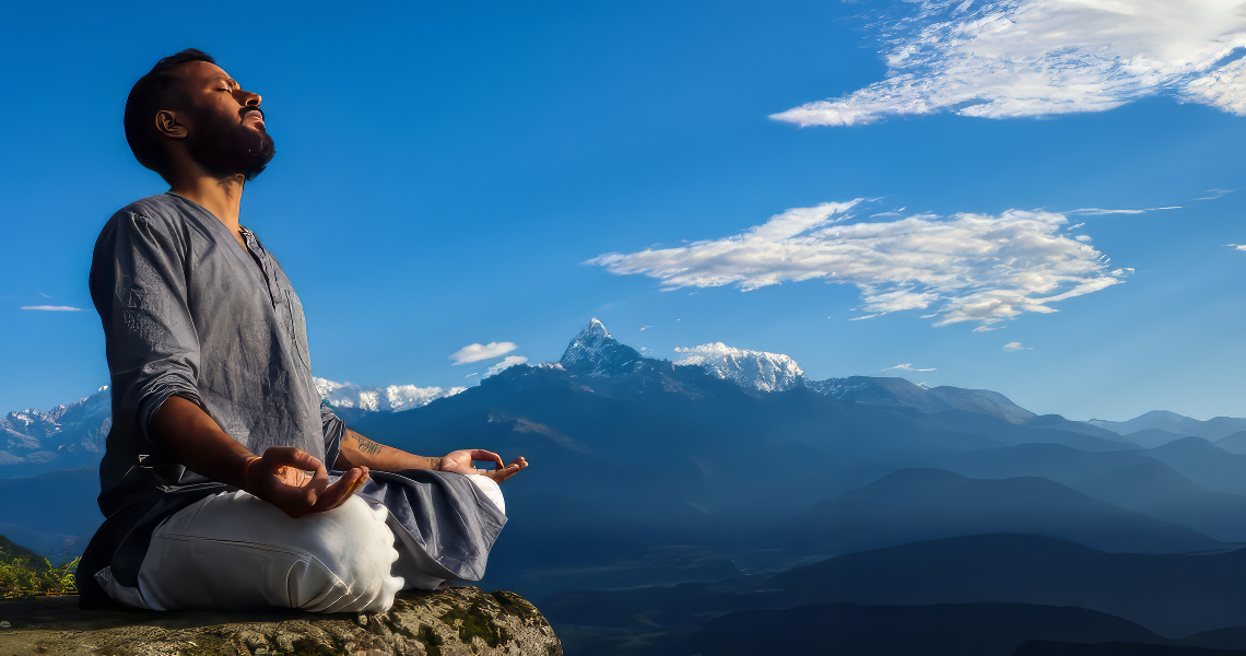 Promisecare Medical Group - Man meditating on a mountain at sunrise with snowy peaks in the background under a clear blue sky.