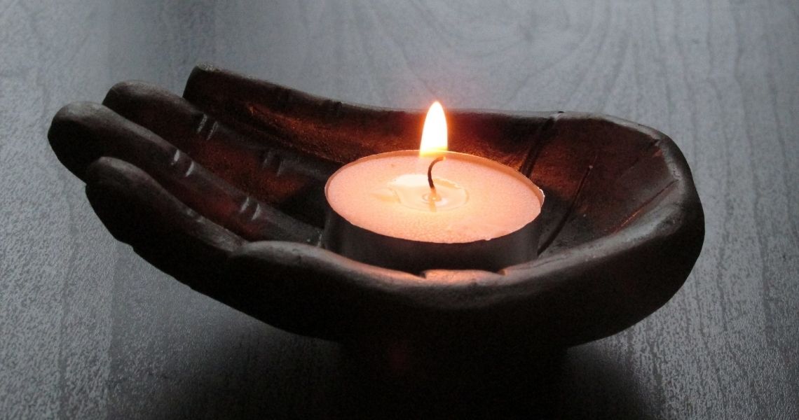 Promisecare Medical Group - A lit tea candle placed in a hand-shaped, brown ceramic holder on a dark surface.