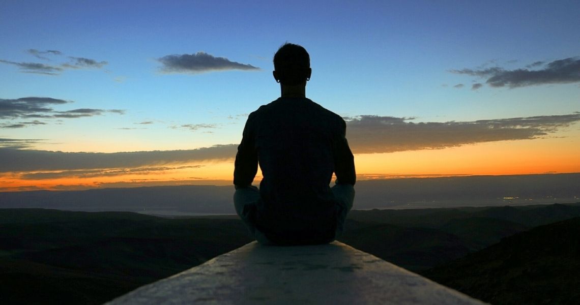 Promisecare Medical Group - Silhouette of a person sitting in meditation at sunrise overlooking a hilly landscape.